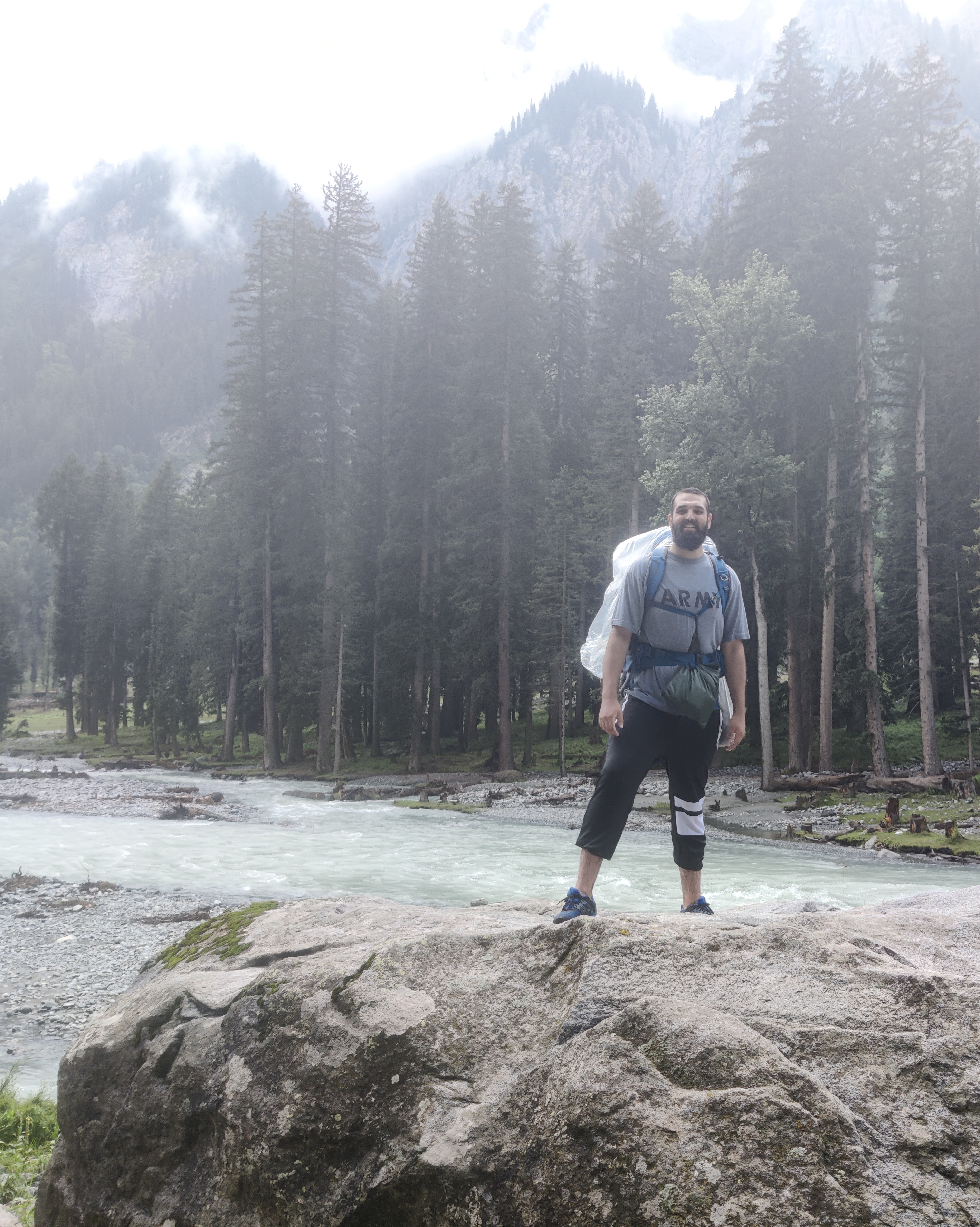 man standing on rock with river and trees behind